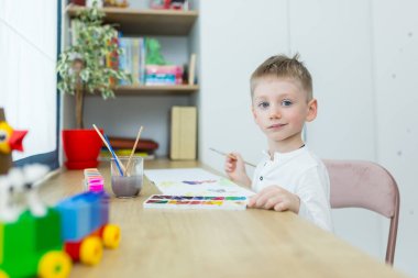 Küçük sarışın çocuk odasında oturmuş, eğleniyor.