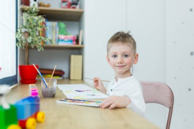 Küçük sarışın çocuk odasında oturmuş, eğleniyor.