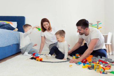 Genç bir aile, iki küçük oğlu olan anne ve baba, çocuk odasında oyuncaklarla oynuyorlar, mutlu bir aile birlikte eğleniyorlar.