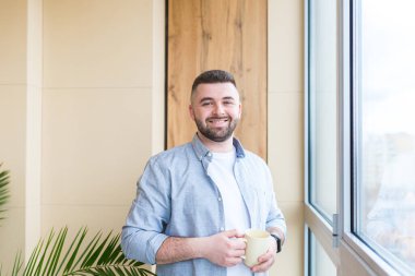 Sakallı yakışıklı adam elinde fincanla pencerede duruyor ve sıcak kahve ya da çay içiyor. Günlük giysiler içindeki erkekler iş yerinde ya da evde manzaranın keyfini çıkarırlar, dinlenirler ya da mola verirler.