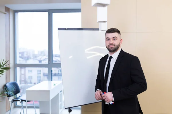 Portrait young bearded man in a formal black business suit with glasses and tie looking at camera. Confident Male a modern office a whiteboard. Manager ceo meeting or conference person, businessman