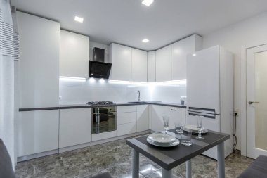 İç mekan fotoğrafı, modern mutfak, açık beyaz renkler, yerde siyah mermer fayanslar, küçük bir daireye yerleştirilmiş.