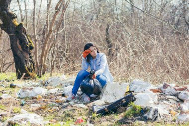 Genç ve güzel bir kadın parkta çöpleri topladıktan sonra yorgun ve dinleniyor. Elinde plastik poşetler var.