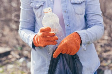 Gönüllü adam park ve ormandaki çöpleri topluyor. Ekoloji konsepti, kadın eli çöp torbasına plastik bir şişe koyar.