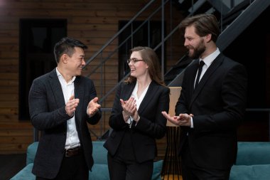  Takım elbiseli iş adamları başarılı bir iş anlaşması planladıktan sonra şirket ofisinde hissedarlarla buluşup dans ediyor ve gülümsüyor. İş, sözleşme