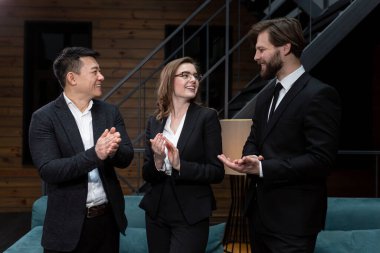  Takım elbiseli iş adamları başarılı bir iş anlaşması planladıktan sonra şirket ofisinde hissedarlarla buluşup dans ediyor ve gülümsüyor. İş, sözleşme