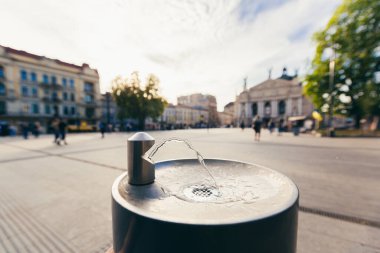 Büyük bir turizm şehrinin arka planında çeşme içmek