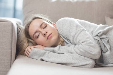 Genç kadın yorucu bir günün ardından kanepede dinlenerek uyuyor. Sakin ol ve dinlen. Yumuşak, rahat bir kanepede. Rahatlık güvenliği. Kapalı gözlü bir kadın sıcakta rahat ve güvende hisseder.