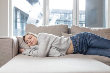 Genç kadın yorucu bir günün ardından kanepede dinlenerek uyuyor. Sakin ol ve dinlen. Yumuşak, rahat bir kanepede. Rahatlık güvenliği. Kapalı gözlü bir kadın sıcakta rahat ve güvende hisseder.