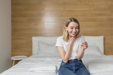 Hamilelik testi yapan mutlu, heyecanlı genç bir kadın neşe dolu sonuçlara bakıyor. Yatak odası, döllenme.