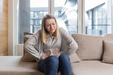 Kanepede oturan genç bir kadın karın üstü el ele tutuşup acıdan, zehirlenmeden ya da regl ağrısından kıvranıyor.