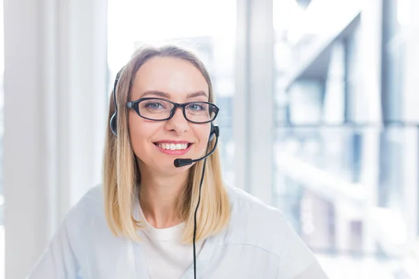 portrait of a woman looking at the camera, young blonde woman with headset and glasses communicates with customers, online consumer support, call center, conference, help close up