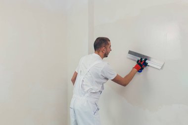 Bir işçi duvarı spatulayla kaplıyor ve çimento karışımı solüsyonu uyguluyor. Tamirci alçıpanı alçıpan üzerine serer..