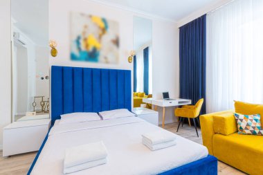 İç mekan fotoğrafçılığı, modern çatı katı tarzında geniş bir yatak odası, çift kişilik yatak ve sarı bir kanepe.