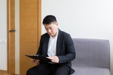 Genç ve başarılı Asyalı bir adam, ofis merkezinin bekleme odasında iş görüşmesini bekliyor, ofis merkezinin resepsiyonunda bir sandalyede oturuyor.