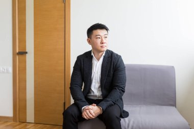 Genç ve başarılı Asyalı bir adam, ofis merkezinin bekleme odasında iş görüşmesini bekliyor, ofis merkezinin resepsiyonunda bir sandalyede oturuyor.