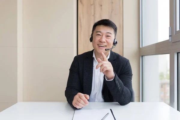 Male businessman conducts an online consultation explains cheerfully gestures with his hands using a headset, and online call