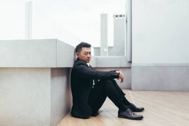 Genç Asyalı bunalımlı adam ofis binasının yanındaki açık havada oturuyor. Üzgün erkek işadamı mali kriz ve karantina yüzünden işini kaybetti. İş adamının sorunları var.