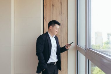 ciddi patron Asyalı iş adamı modern bir ofis merkezinde telefonla konuşuyor, iş arkadaşlarına iş görüşmesi yapıyor.