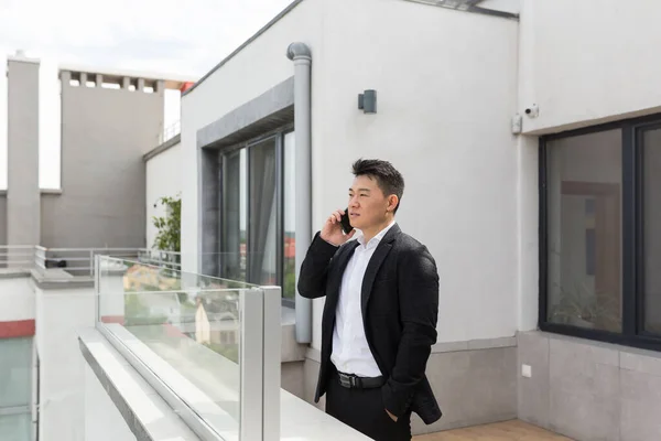 Freelancer Asian businessman in business suit enjoys phone standing on balcony terrace of modern office center