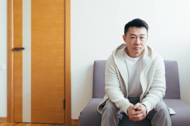 Genç Asyalı bir adam görüşme ya da toplantı için bekleme odasında bekliyor. Sınav ya da istihdam resepsiyonuna katılan öğrenci ya da katılımcı. Ofisteki erkek hasta, hastane ya da klinik.