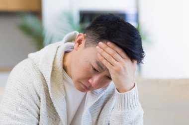 Genç Asyalı bir adam evdeki kanepede oturmuş sorunlardan ve depresyondan endişe ediyordu. Erkeklerin iş ya da aile ilişkileri, kredi geri ödeme borçlarıyla ilgili sorunları vardır.