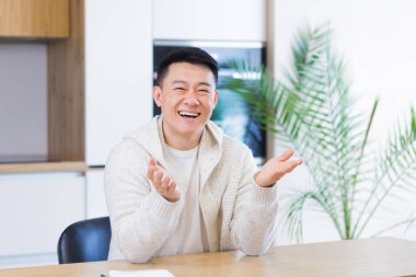 Asyalı bir adam, video odasında kulaklıkla konuşuyor. Sıradan giyinmiş bir erkek kameraya, toplantıya ya da uzaktan konferansa bakıyor. Portre öğrencisi ya da öğretmen eğitimi. Web kamerası görünümü