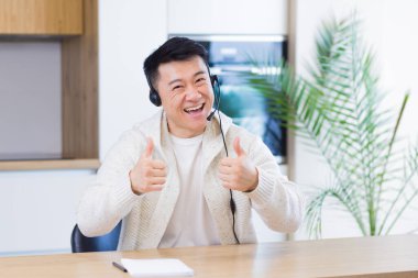 Asyalı bir adam, video odasında kulaklıkla konuşuyor. Sıradan giyinmiş bir erkek kameraya, toplantıya ya da uzaktan konferansa bakıyor. Portre öğrencisi ya da öğretmen eğitimi. Web kamerası görünümü