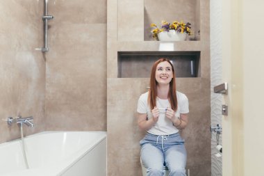 Mutlu beyaz kadın hamilelik testi pozitif çıkınca sevinçten havalara uçuyor. Evdeki kadın portresini yakından çek. Sonuçları kontrol et ve heyecanla tuvalette otur. Mutluluk