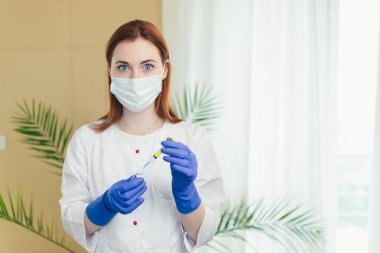 Kadın doktor aşıları enjekte edilir, ciddi hemşire kameraya bakar ve yüzünde koruyucu bir maske takılır.