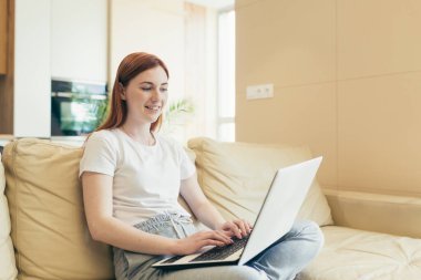 Genç ve güzel bir kadın. Evde çalışıyor. Kanepede oturuyor.