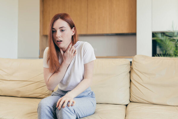 Young woman alone at home with a panic attack shortness of breath, trembling, numbness, loss of consciousness. Front view of a female suffering an anxiety sitting on a couch. chest pain, fear symptom