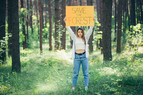 young beautiful woman volunteer activist in the forest with a poster save the forest