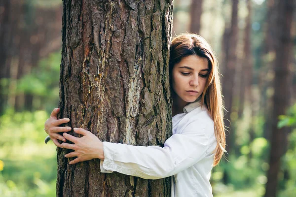 Young beautiful female volunteer hugs a tree with love in the forest
