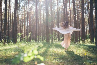 Genç ve güzel hippi kadın yaz ormanında yürüyor gülüyor, dans ediyor ve hayatın ve doğanın tadını çıkarıyor.