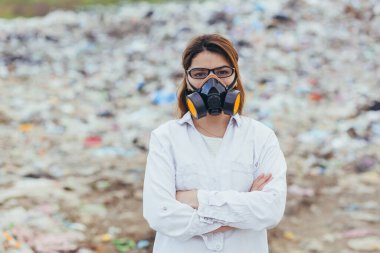 Çöp sahasında koruyucu solunum maskesi takan kadın bilim adamı, çevre kirliliğinin seviyesini değerlendiriyor