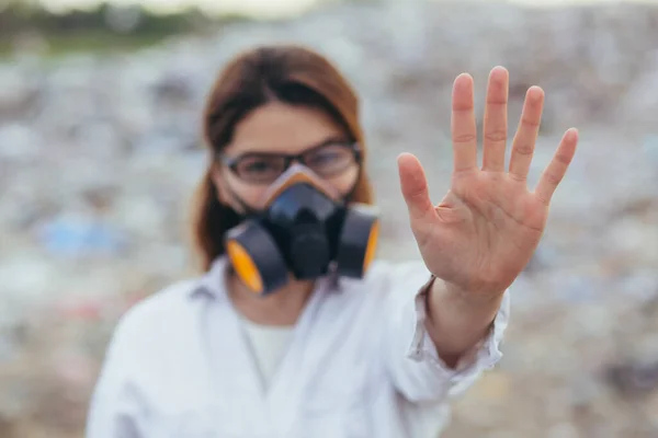 A woman in a protected respiratory suit at landfills, holding hands in front, trying to stop the pollution of the planet, shows a stop sign with her hands
