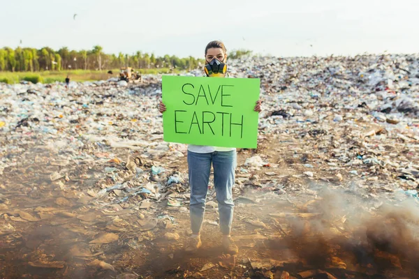 Woman with a poster save the planet, pickets garbage-contaminated environment, burning fire and black smoke