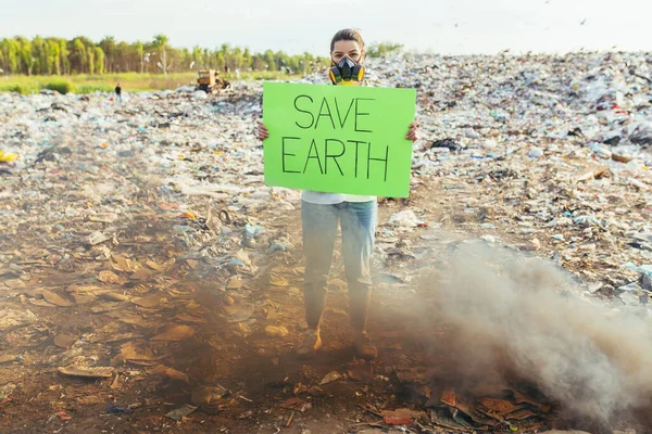 Woman with a poster save the planet, pickets garbage-contaminated environment, burning fire and black smoke
