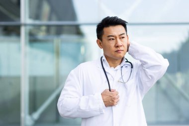 Asyalı doktor işten sonra yorgun, depresyonda ve kliniğin yakınındaki sokakta yapılan işten dolayı hayal kırıklığına uğramış.