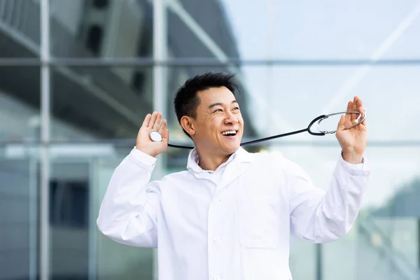一位快乐的亚洲医生的画像 他跳舞时对在外面一家现代诊所的背景下所做的工作结果感到满意 — 图库照片