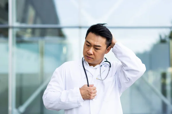 Asian doctor is tired after work, depressed and disappointed with the work done on the street near the clinic