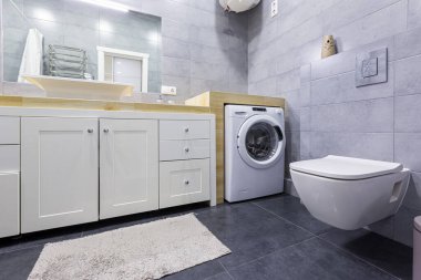 Küçük bir dairede gri fayanslı modern bir banyonun iç mekan fotoğrafı.