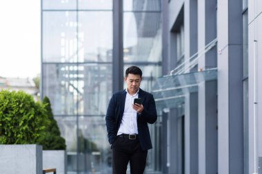 Başarılı Asyalı patron telefonda iş elbisesi içinde ciddi bir şekilde yazışmış.