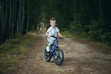 Küçük bir çocuk ormanda bisiklet sürüyor.