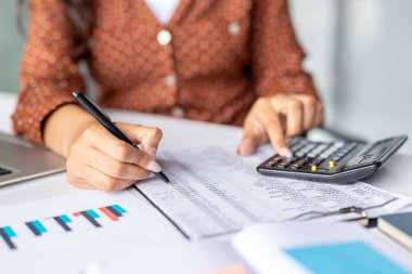 Close-up of accountants hands using calculator and taking notes while analyzing financial reports with charts and graphs, performing accounting tasks in office