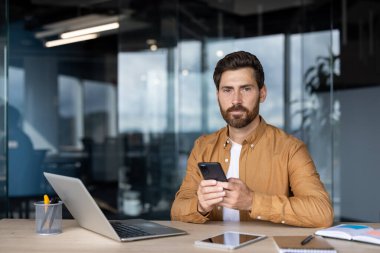 Modern ofis ortamında çalışan bir adam, profesyonel bir iş ortamında iletişim, teknoloji ve üretkenliği temsil eden bir akıllı telefon kullanırken işine odaklandı.