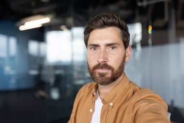 Kendine güvenen sakallı adam kameraya bakıyor. Video görüşmesi yapıyorum. Ya da arka planda bulanık cam duvarlar olan kapalı bir ofis çalışma alanından selfie çekmek gibi. Profesyonelliği ve bağlantıyı temsil etmek