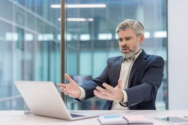 Modern ofisteki stresli işadamı kafa karışıklığı ve hayal kırıklığı yaşıyor, bir dizüstü bilgisayara güvensizlik ve endişe dolu bir bakış atıyor.