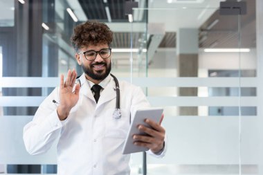 Beyaz önlüklü ve steteskoplu bir doktor dijital tablet üzerinden uzaktan tıbbi konsültasyon ya da çevrimiçi bir sınıf yürütüyor.